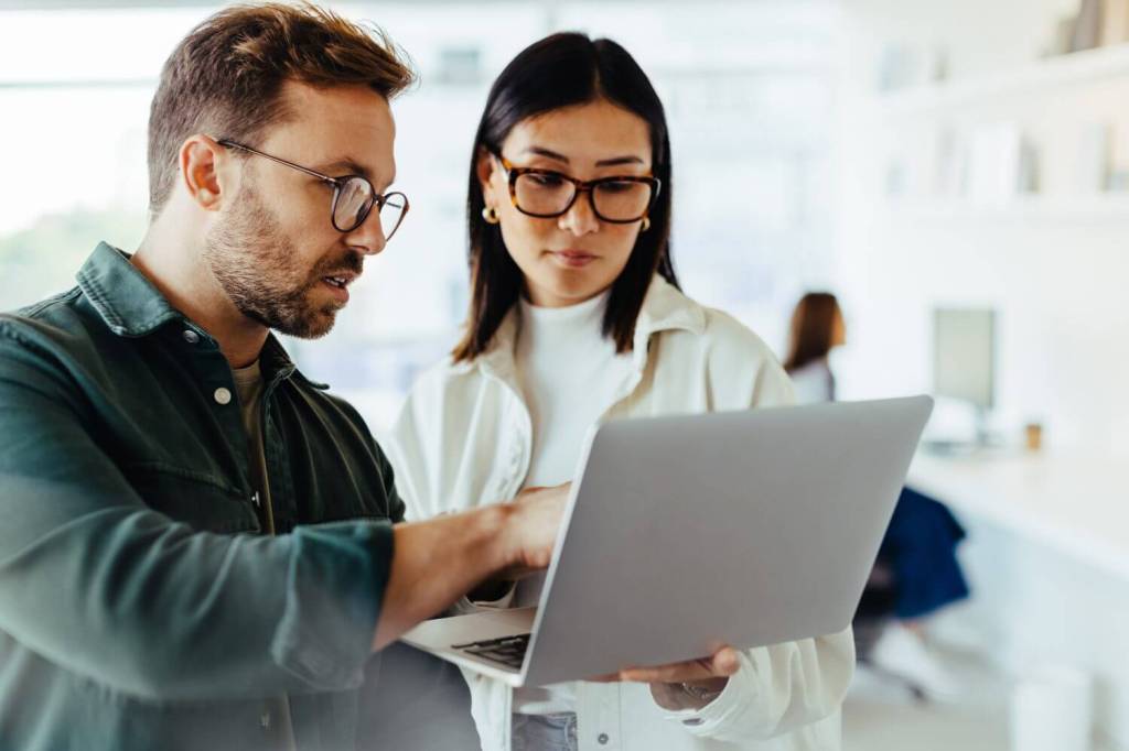 A man and a woman look at a laptop together while working