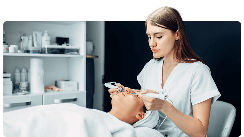Beauty therapist performing a procedure on a client lying on a bed.